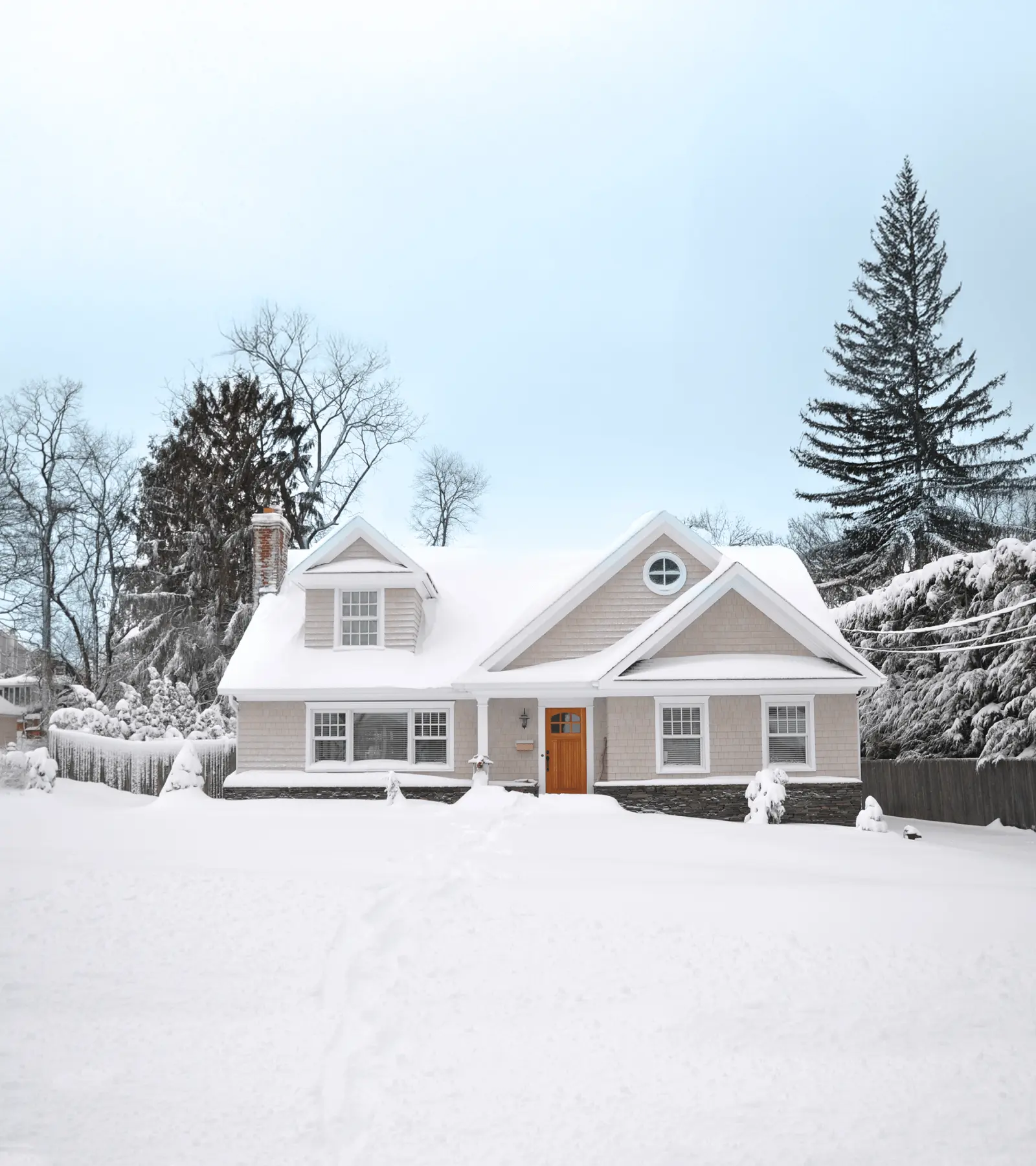 Exterior shot of a two story house with snow on the roof and ground. Pine trees in the background.