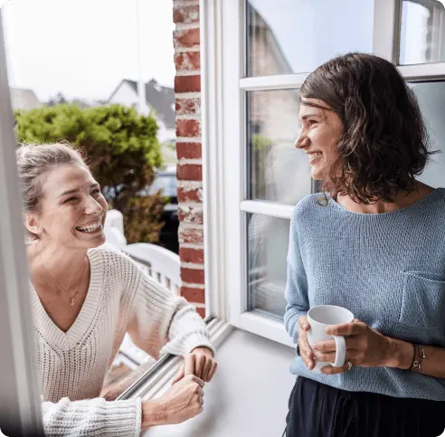 Two women laugh and have a conversation by a window