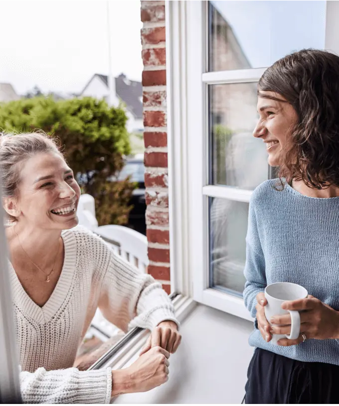 Two women laugh and have a conversation by a window