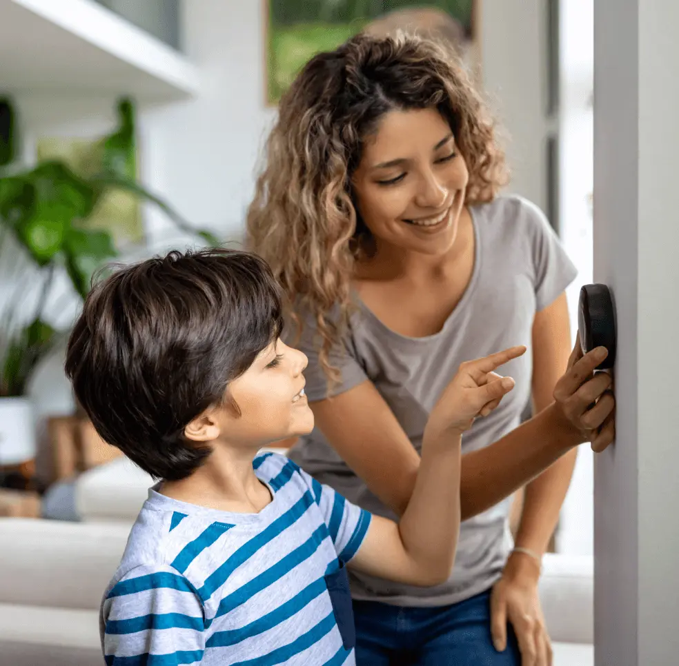 Woman and child adjust thermostat on the wall.