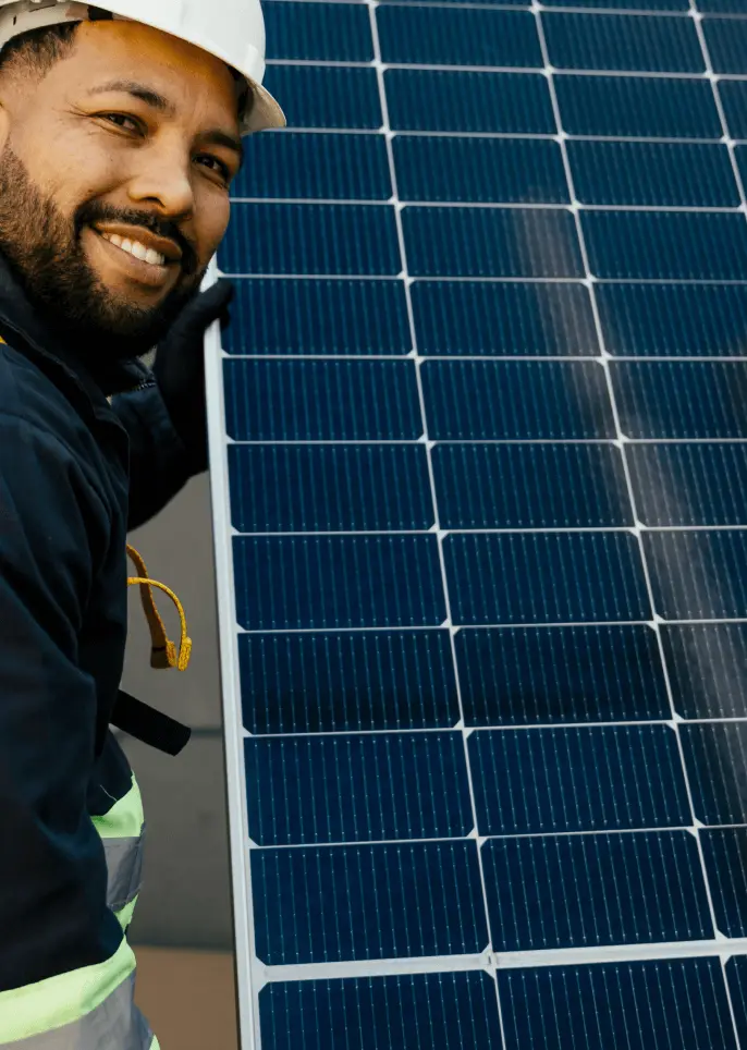 A worker wearing safety gear holds a solar panel